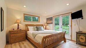Een slaapkamer met een houten bed, nachtkastjes, een dressoir, een televisie en een schuifdeur die uitkomt op een tuin.
