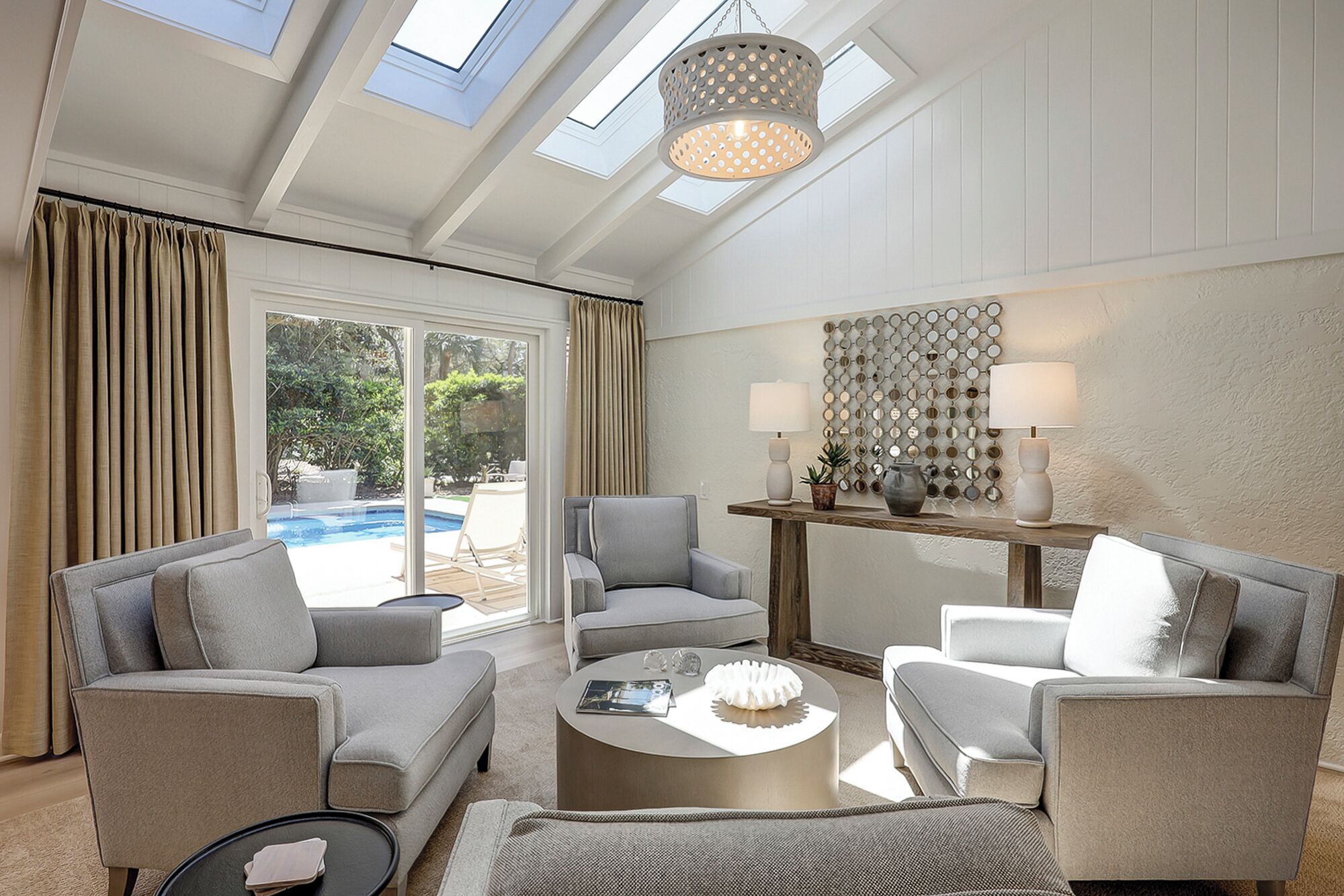A spacious living room with a pool view, grey sofas, a coffee table, and a decorative wall.