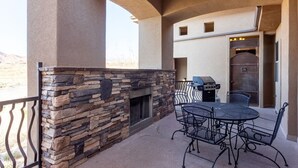 Un patio con chimenea de piedra, parrilla al aire libre y mesa y sillas de metal.