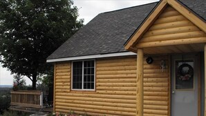 Eine Blockhütte mit Satteldach, einer Veranda und einem kleinen Fenster.