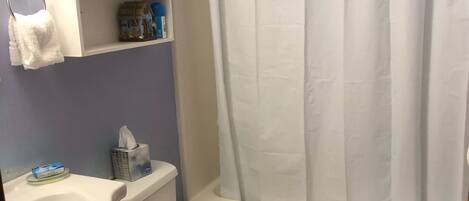 Un baño con inodoro, lavamanos y bañera. Hay un perchero sobre el lavamanos y una cortina de ducha en la bañera.