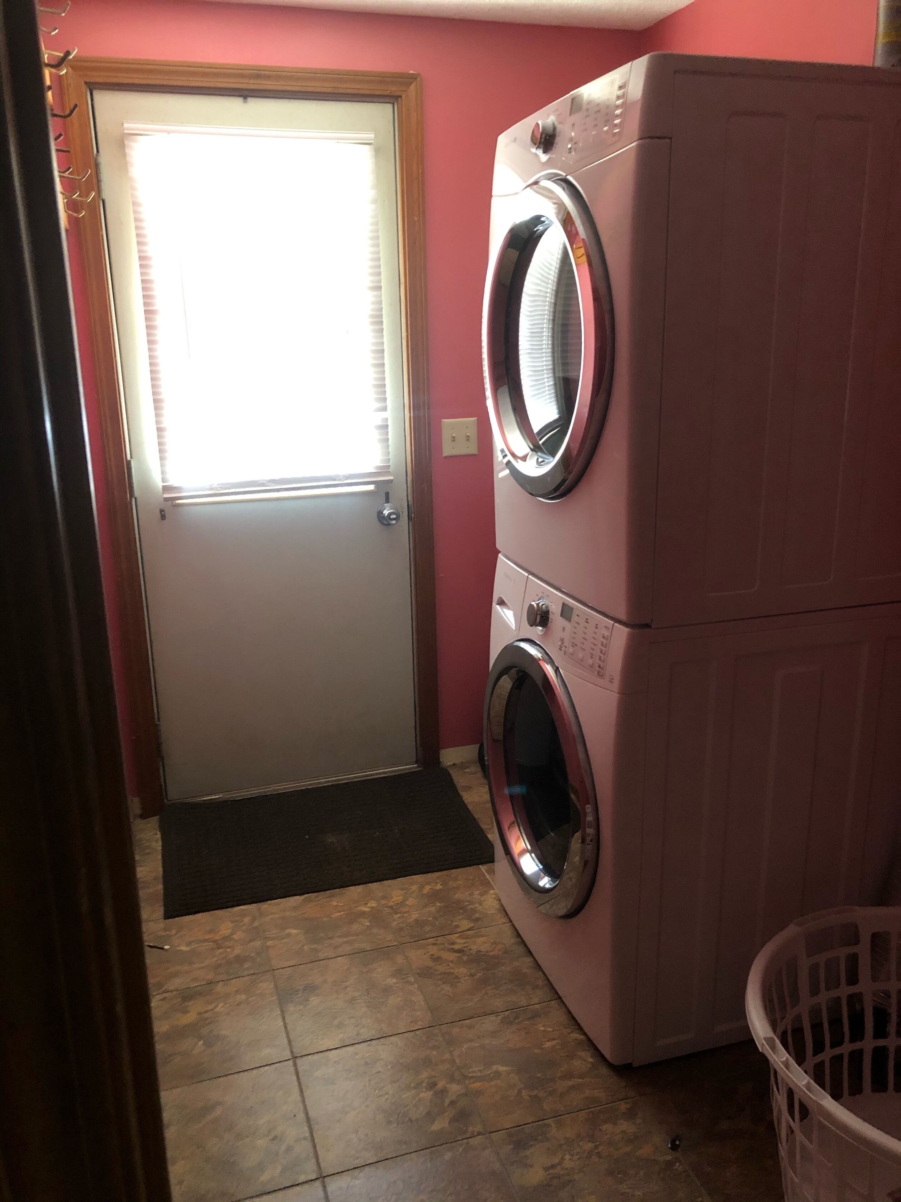 A laundry room with a washing machine and dryer, a door with a window, and a mat at the entrance.