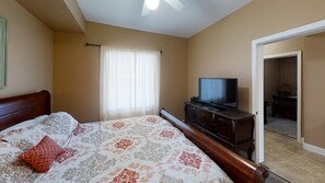 Un dormitorio con cama, televisor sobre un tocador y puerta que da a otra habitación.