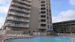 A high-rise hotel with a swimming pool, multiple balconies, and a parking garage in the background.