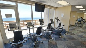 A gym with exercise equipment, large windows with a view of the ocean, and a "No Exit" sign.