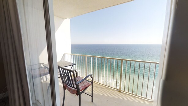A balcony with a view of the ocean, a chair, and a table.