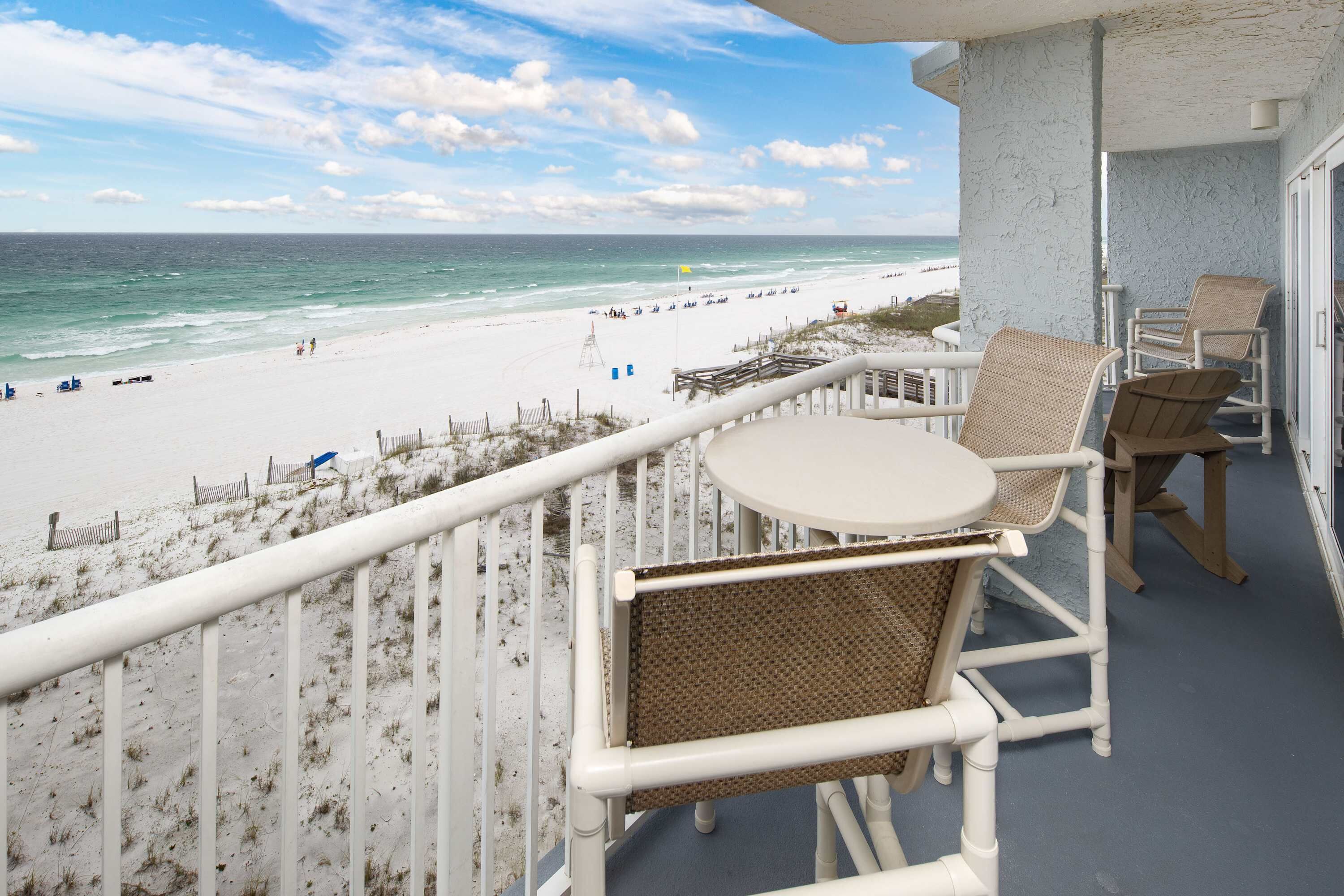 Een balkon met uitzicht op het strand, wit rieten meubilair en een klein tafeltje.