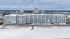 A large hotel with multiple floors and balconies, situated near a beach with a pier extending into the water.