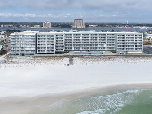 A large hotel with multiple floors and balconies, situated near a beach with a pier extending into the water.