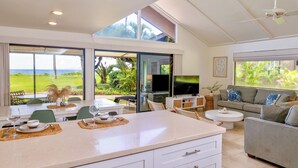 A modern kitchen with a dining area, a living room with a sofa, and a TV. There is a large window with a view of the outdoors. - Ma'alaea Surf Unit C1 Beachfront Condo, 2BR Ground Floor, AC, Wifi, Kitchen (Kihei)