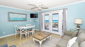 A living room with a dining table, chairs, a coffee table, a TV, a ceiling fan, a sofa, a lamp, and a view through the glass door. - Cozy 1 Bedroom🏝️ Gulf Views🌊Summerspell 309 (Miramar Beach)