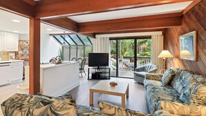 A spacious living area with a wooden ceiling, a large TV, a sofa, and a dining area with a kitchen in the background. - Beachwalk 174 - Shipyard 3BR/3.5 BA Townhouse (Hilton Head Island)