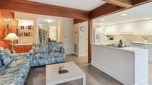 A living room with a sofa, coffee table, and a kitchen area with white cabinets and appliances. - Beachwalk 174 - Shipyard 3BR/3.5 BA Townhouse (Hilton Head Island)