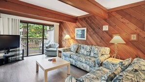 A cozy living room with a wooden ceiling, a flat-screen TV, a sofa, a coffee table, and a lamp. - Beachwalk 174 - Shipyard 3BR/3.5 BA Townhouse (Hilton Head Island)