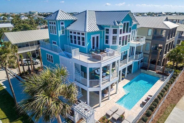 A large, multi-story house with a swimming pool, multiple balconies, and a view of the surrounding area.
