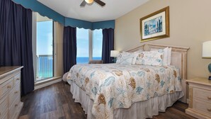 Quarto com cama grande, penteadeira, mesa de cabeceira e vista para o oceano.