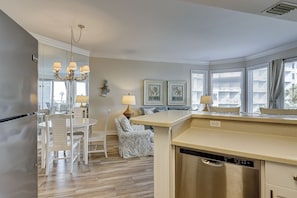 A kitchen with a dishwasher, a dining area with chairs and a table, and a chandelier.