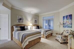 A bedroom with two beds, a window with blinds, a chair with a starfish pattern, and a painting of a sailboat.