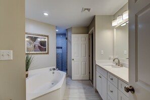 A modern bathroom with a bathtub, a large mirror, and a door leading to another room.