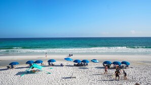 A beach with white sand, clear blue water, and several blue umbrellas. - "Sunseekers 2" | Beachfront | Ground Floor with Open Greenspace, and Amazing Views (Santa Rosa Beach)