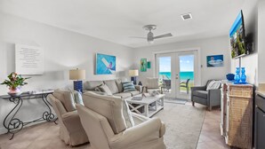 A living room with a sofa, chairs, a coffee table, a TV, and a view of the ocean through the sliding glass door. - "Sunseekers 2" | Beachfront | Ground Floor with Open Greenspace, and Amazing Views (Santa Rosa Beach)