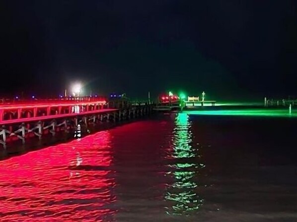 Un muelle con un camino que se extiende sobre el agua, iluminado por luces rojas y verdes.