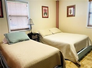 Una habitación con dos camas, una mesita de noche con lámpara y dos cuadros enmarcados en la pared.