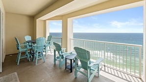 Un balcone con sedie Adirondack color turchese e un tavolo, con vista su una spiaggia e l'oceano.