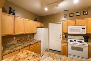 A kitchen with granite countertops, wooden cabinets, a white refrigerator, a microwave, and a stove.