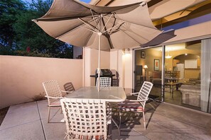 An outdoor patio with a table and chairs, a grill, and a large umbrella.