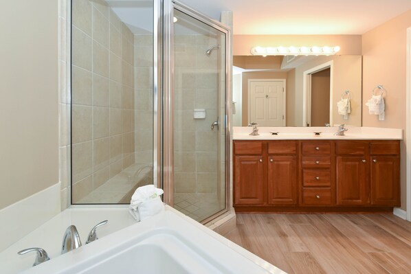 Une salle de bain moderne dotée d’une douche à parois de verre, d’un meuble-lavabo à deux vasques, d’armoires en bois et d’un grand miroir avec des lumières au-dessus.