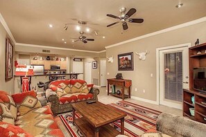 Una sala de estar con sofá, mesa de centro y mueble para televisión. Se ve una cocina al fondo.