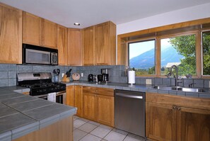 Una cocina con armarios de madera, un lavavajillas de acero inoxidable y un ventanal con vistas a la montaña.