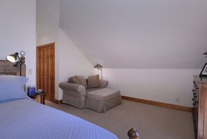 Ein Schlafzimmer mit Bett, Nachttisch, Kommode, Sessel und Lampe.