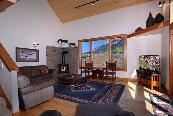 Una sala de estar acogedora con chimenea de piedra, un ventanal con vistas a la montaña y un televisor.