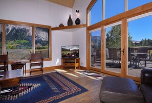 Una sala de estar con televisión, muebles de madera, un ventanal y vistas a un paisaje montañoso.