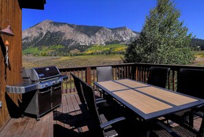A deck with a grill, table, and chairs, overlooking a mountainous landscape. - The 8th Green of the Club at CB!  Dog Friendly! (Crested Butte)