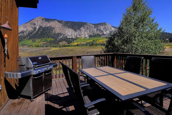 Una terraza con una parrilla, mesa y sillas, con vista a un paisaje montañoso.