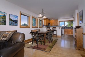 Amplia sala de estar con sofá de cuero, comedor con sillas de madera, cocina con gabinetes de madera y ventanas grandes que ofrecen vistas al exterior.