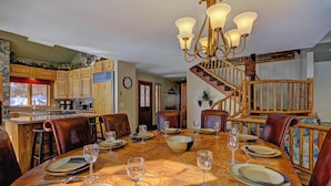 A dining area with a wooden table set for six, surrounded by leather chairs. A chandelier hangs above the table, and a wooden staircase is visible in the background. - Free SkyCard Activities - Private Hot Tub, Ideal for Families - Gold King Lodge (Breckenridge)