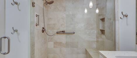 A modern bathroom with a glass shower enclosure, a handrail, and a marble countertop.