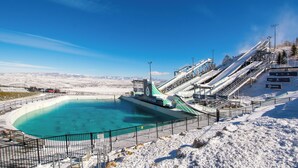 Une piste de ski enneigée, avec une piscine d’eau cristalline à son pied, entourée de clôtures et de remontées mécaniques.