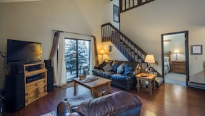 Un salon comprenant un téléviseur, un meuble de rangement en bois, un canapé en cuir et un escalier orné de vitraux.