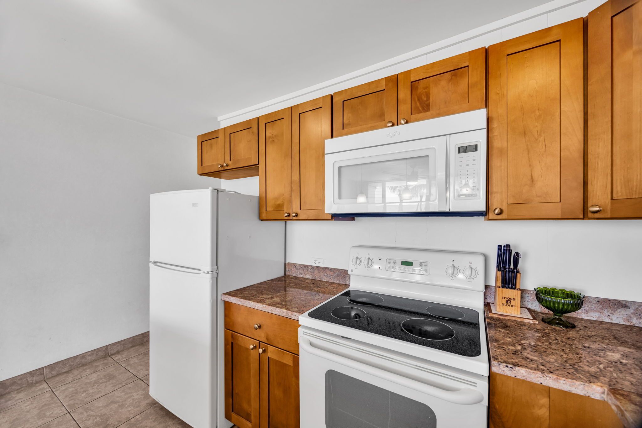 A kitchen with wooden cabinets, a white refrigerator, a microwave, and a stove.