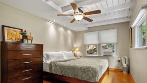 Une chambre à coucher avec un lit, une commode en bois, un ventilateur de plafond et des fenêtres.