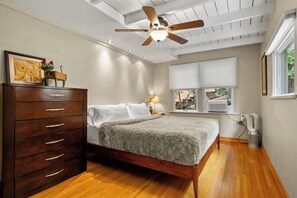 Una camera da letto con un letto, una cassettiera in legno, una ventola a soffitto e finestre.
