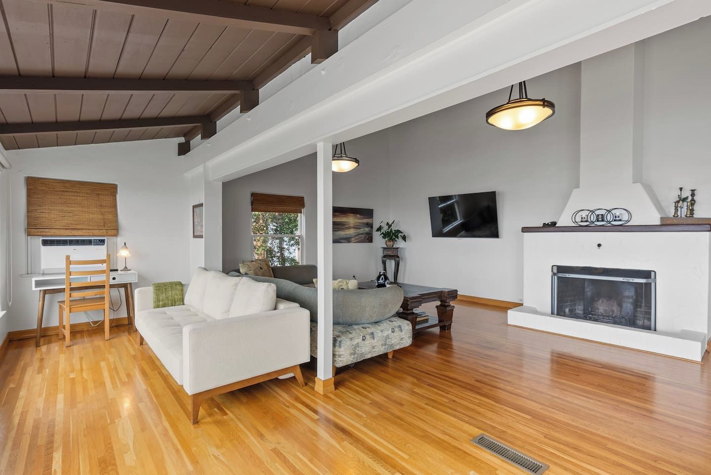 A spacious living room with a fireplace, wooden flooring, and a seating area with a sofa and armchairs.