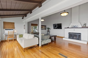 A spacious living room with a fireplace, wooden flooring, and a seating area with a sofa and armchairs. - Hilltop Oasis Panoramic Views! (San Diego)