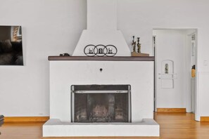 A modern fireplace with a white mantel and a glass door, set in a room with wooden flooring and a white wall.