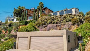 Une propriété résidentielle dotée d’un garage, d’une colline couverte de végétation et d’un ciel bleu dégagé.